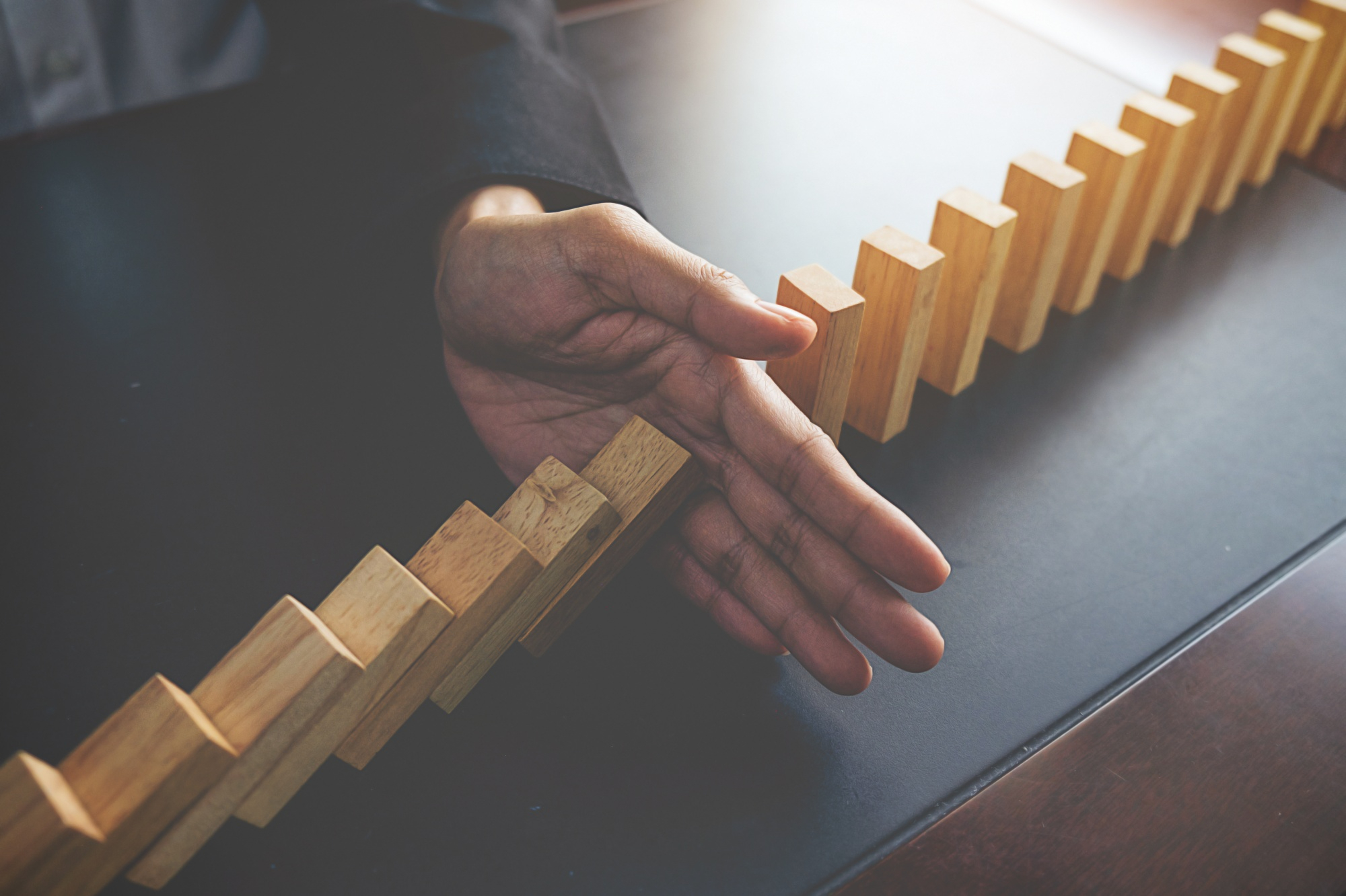 a person putting their hand down between falling dominoesa person putting their hand down between falling dominoes