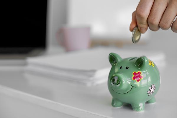 close up of hand putting coin in green piggy bank